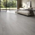 Clash Wood Grey Wood Look Tile in a modern bedroom featuring light grey wood-grain plank flooring, neutral décor, and large glass windows.