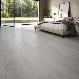 Clash Wood Grey Wood Look Tile in a modern bedroom featuring light grey wood-grain plank flooring, neutral décor, and large glass windows.